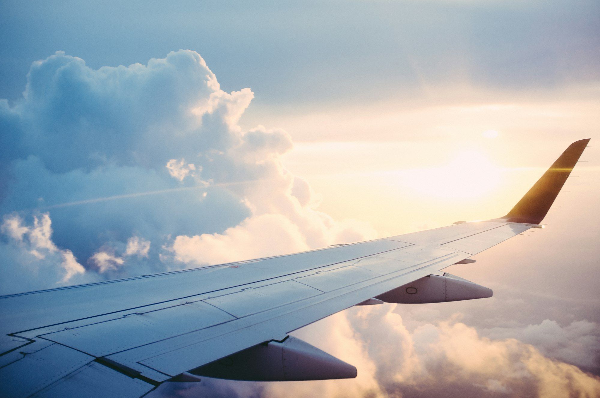 View from an aircraft window of a wing above sunlit clouds