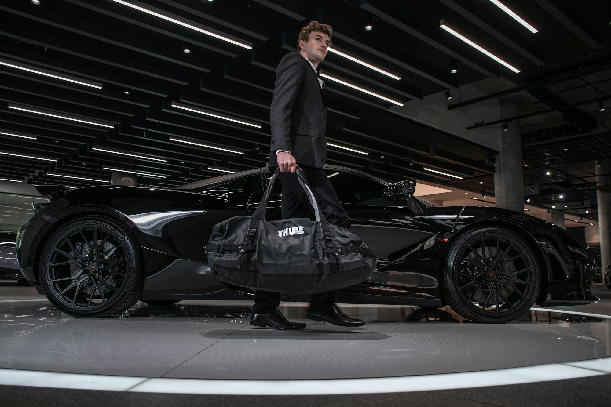 A chauffeur in a dark suit walking past a black luxury car